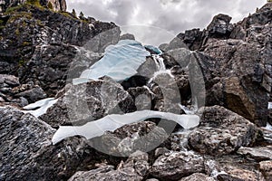 Huge boulders through which a mountain stream flows and the remains of ice on the stones.