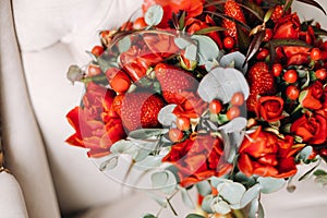 A huge bouquet of beautiful red roses with strawberries lies on the chair