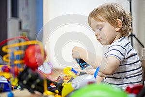 A huge bunch of different and colored toys in front of playful child. Little kid is playing toys in children`s room