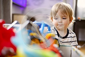 A huge bunch of different and colored toys in front of playful child. Little kid is playing toys in children`s room