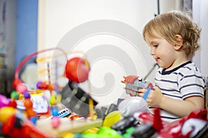 A huge bunch of different and colored toys in front of playful child. Little kid is playing toys in children`s room