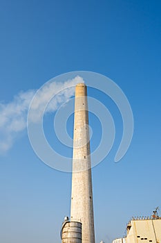 A huge chimney of a modern industrial factory against blue sky