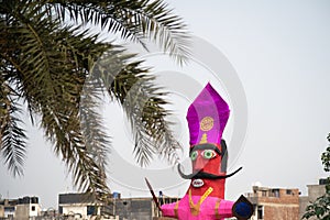 Huge colorful ravana effigy with a sword and a shield placed on the side of a busy street with a tree in the foreground