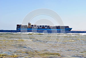 A huge container ship carries many commercial containers. Side view from the shore