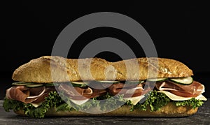 Huge crispy baguette sandwich with meat and vegetables. Close up.