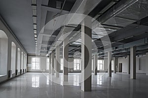 Huge empty open space in the old factory building with rows of columns, large windows and pipes under the ceiling