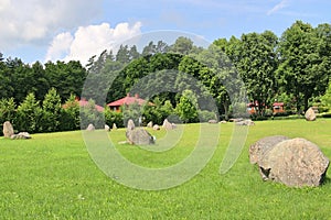 Huge erratic boulders in the megalith park. Big stones lie in the green grass. There are green trees around. Silvarium, a forest p