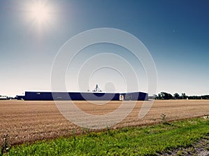 Huge farm building by a field on a warm sunny day with blue cloudy sky. Agriculture industry. Food supply chain. Grain product