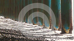 A huge foamy sea wave beats through metal columns on a rocky beach