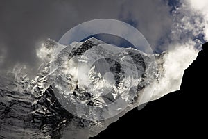 A huge glacier from a very high mountain appears among the clouds in the annapurna of the nepali himalayas