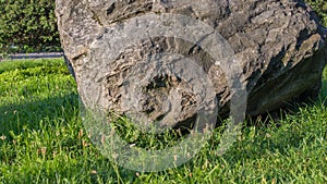 Huge gray volcanic diorite stone with rough edges lying on the lush green grass on a fine sunny day