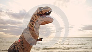 Huge inflatable dinosaur on beach at sunset waves paws says hello and runs away.