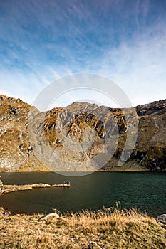 Huge lake in the mountains with a little house on the dock. Nice blue sky with some clouds.  Vertical shot.