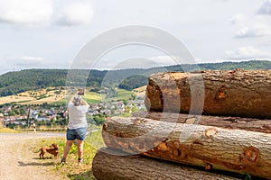 Huge logs on hill, hiker taking a photo standing next to dog, German rural landscape in background photo
