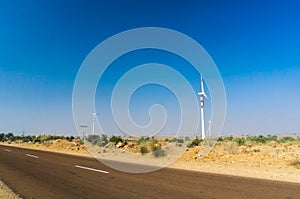 Huge modern windmill on hills with buildings in front and blue sky behind.