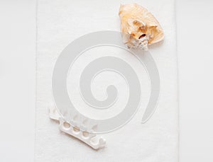 Huge natural seashell on a white towel and pedicure finger separator. Personal care at home