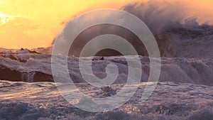 Huge ocean surf crashing over rocks at sunset