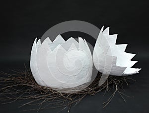 Huge papier mache egg in a nest of branches is uncovered in two parts on a black background