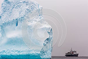 Huge piece of iceberg with antarctic cruise ship at the horizon, Antarctica