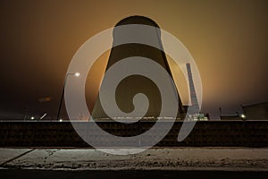 Huge pipe of thermal power station at night on the background of clouds in the sky and urban light