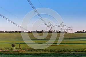 Huge power line towers on field at summer evening