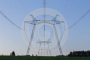 Huge power line towers on field at summer evening