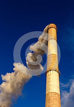 Huge red and white chimney rising high above towards a blue sky belches out v