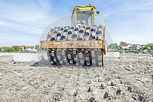 Huge road roller with spikes is compacting soil at construction