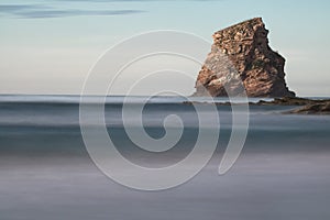 Huge rock cliff isolated in ocean in long exposure in sunset sky, hendaye, basque country, france