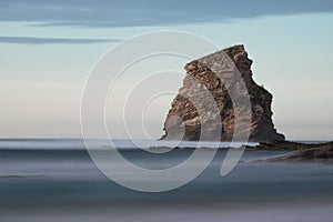 Huge rock cliff isolated in ocean in long exposure in sunset sky, hendaye, basque country, france