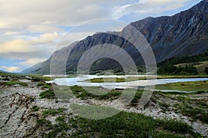 A huge rocky mountain range in the valley of the Akkol river in Altai, with a river and a clay bank with grass, with beautiful