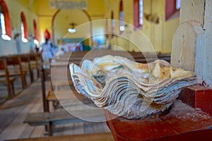 Huge seashell as a bowl for sacred water in Catholic church. Empty seats in the holy mass hall