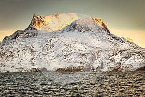 Huge Sermitsiaq mountain in a sunset rays covered in snow with blue sea and small fishing boat, nearby Nuuk city, Greenland