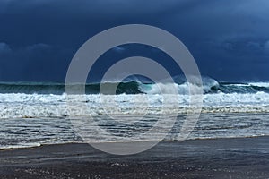 Huge shore breaking wave with distant storm