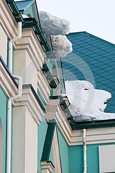 A huge snow block hangs from the roof above the entrance to the building.