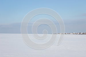 Huge snow covered field leading to the village under the blue sky