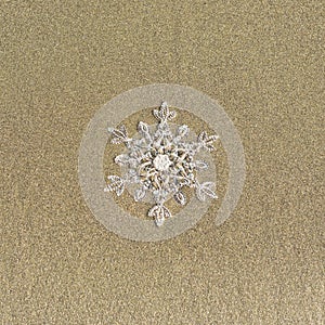 Huge sparkling snowflake on the sand in the sea foam. Concept of Winter and Christmas vacation on the beach