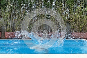 A huge splash of water is created by the cannonball dive into a swimming pool