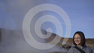 The huge Strokkur geyser erupts behind the girl