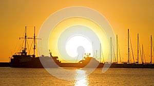 A huge sun, a jetty, harbor with big ship and yachts on the sunset background.
