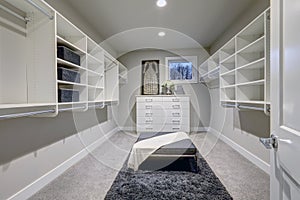 Huge walk-in closet with shelves, drawers and gray bench.