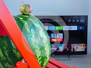 Huge watermelon and tiny apple watching TV set