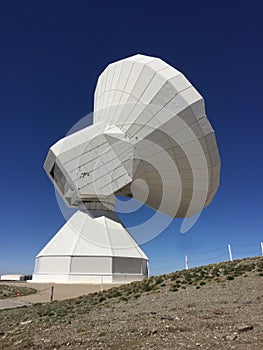 Huge white antenna radio telescope on blue sky background on top of the mountain