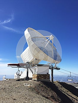 Huge white antenna radio telescope on blue sky background on top of the mountain