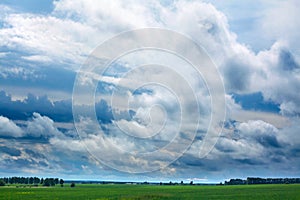 Huge white clouds in the blue sky above the green field