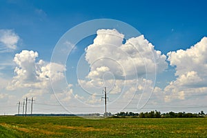 Huge white clouds in the sky over green fields, trees, forests. Electric poles