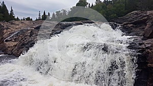 Huge white waterfall rushes down a rocky hillside