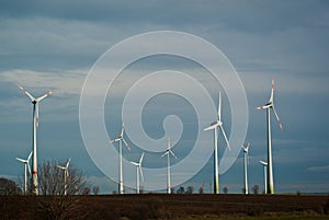 Huge white windmills stand against the grey sky in clouds.