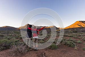 Hugging couple with outstretched arms watching the stunning view of the Karoo National Park at sunset, travel destination in South