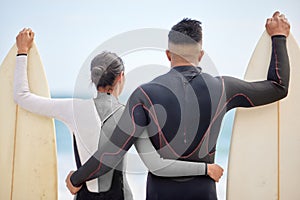 Hugging, couple and surfboard on beach with swimwear, together and watching waves for wellness, exercise and bonding
